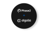black circle with a white Phase2 logo on the top, a blue plus sign in the middle and a white Algolia logo at the bottom.